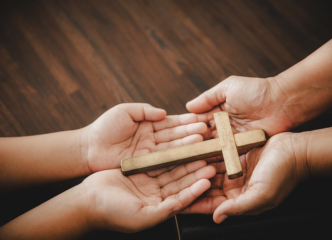 Bild von vier Händen, die ein Kreuz halten