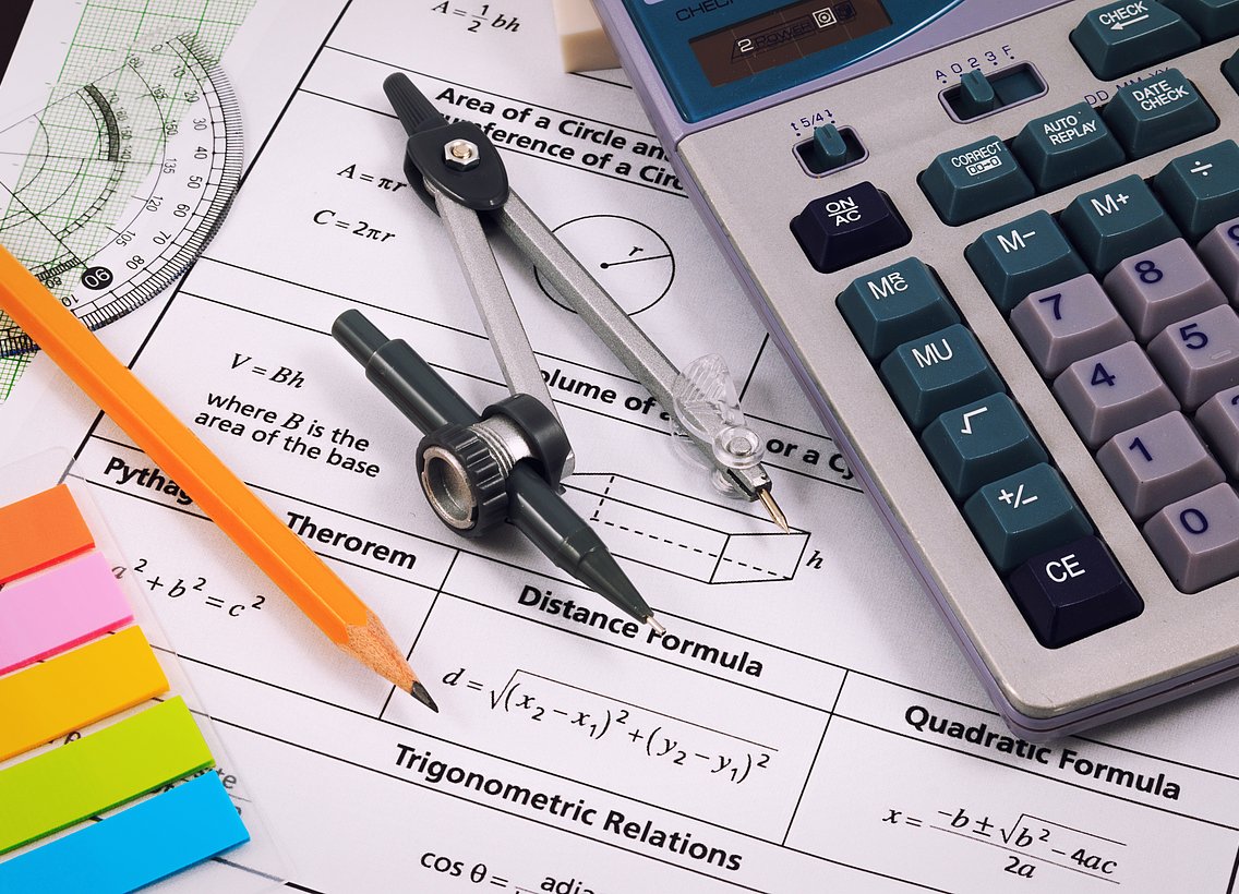 Bild von einem Schreibtisch mit Taschenrechner und Zirkel